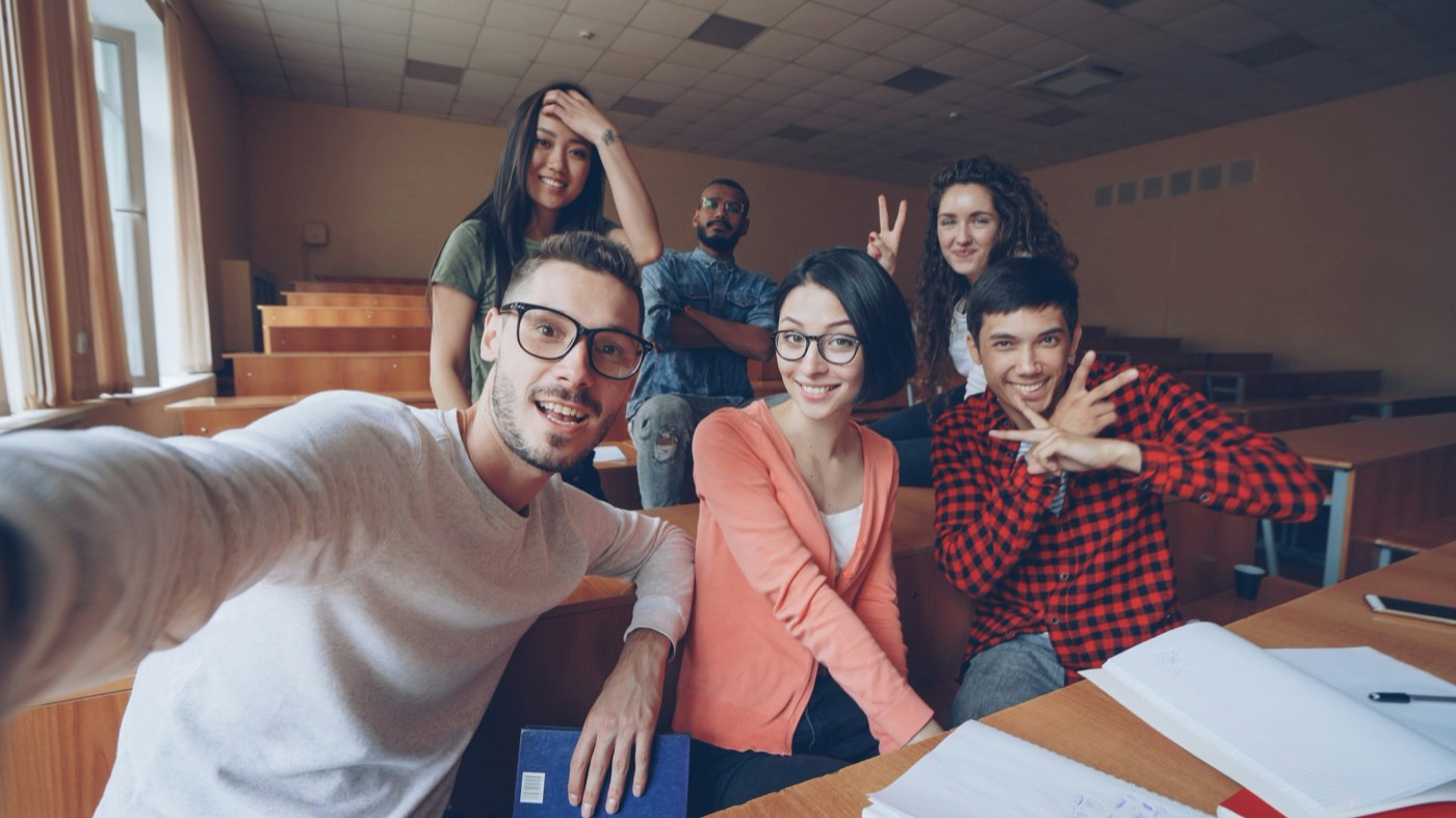 A group of young adults smiling for a selfie in a lecture hall