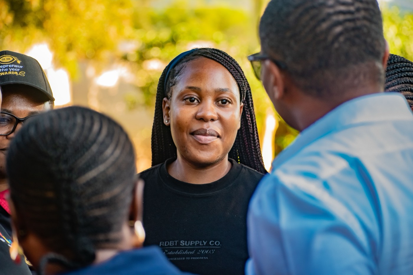 A woman in a black t-shirt speaking with two attendees at an outdoor event