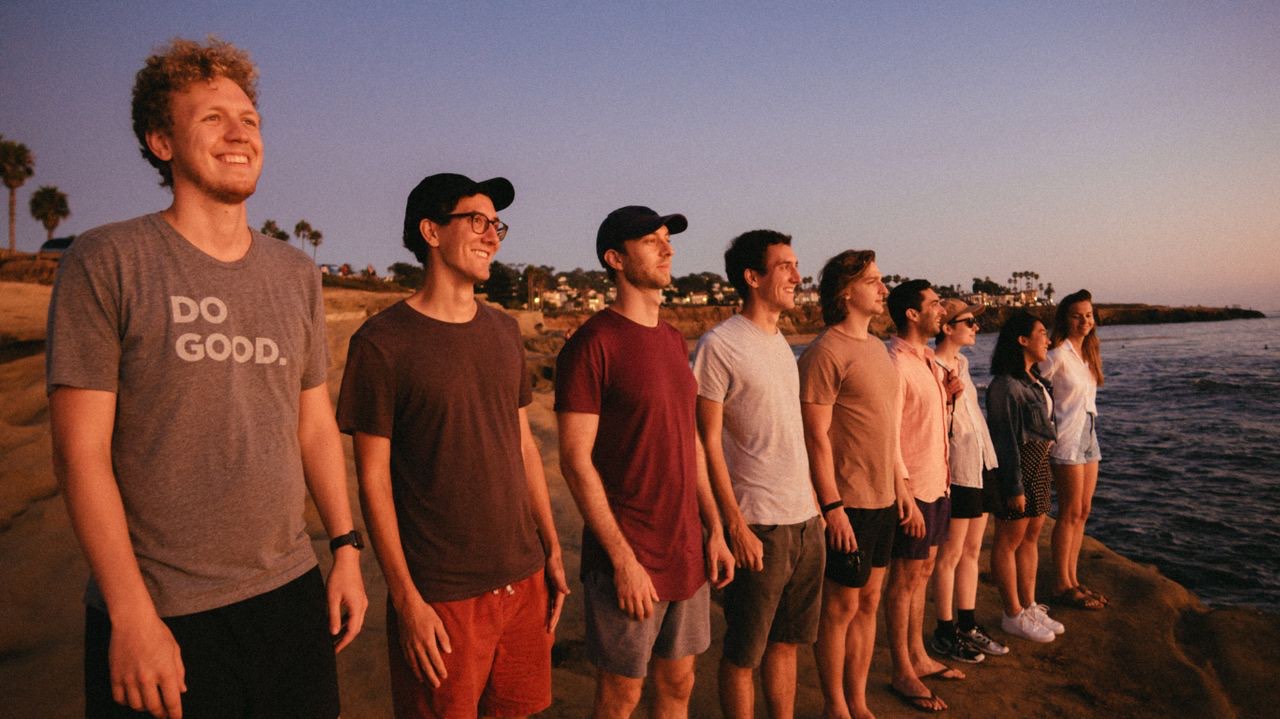 Young volunteers in matching t-shirts lined up facing the water at sunset
