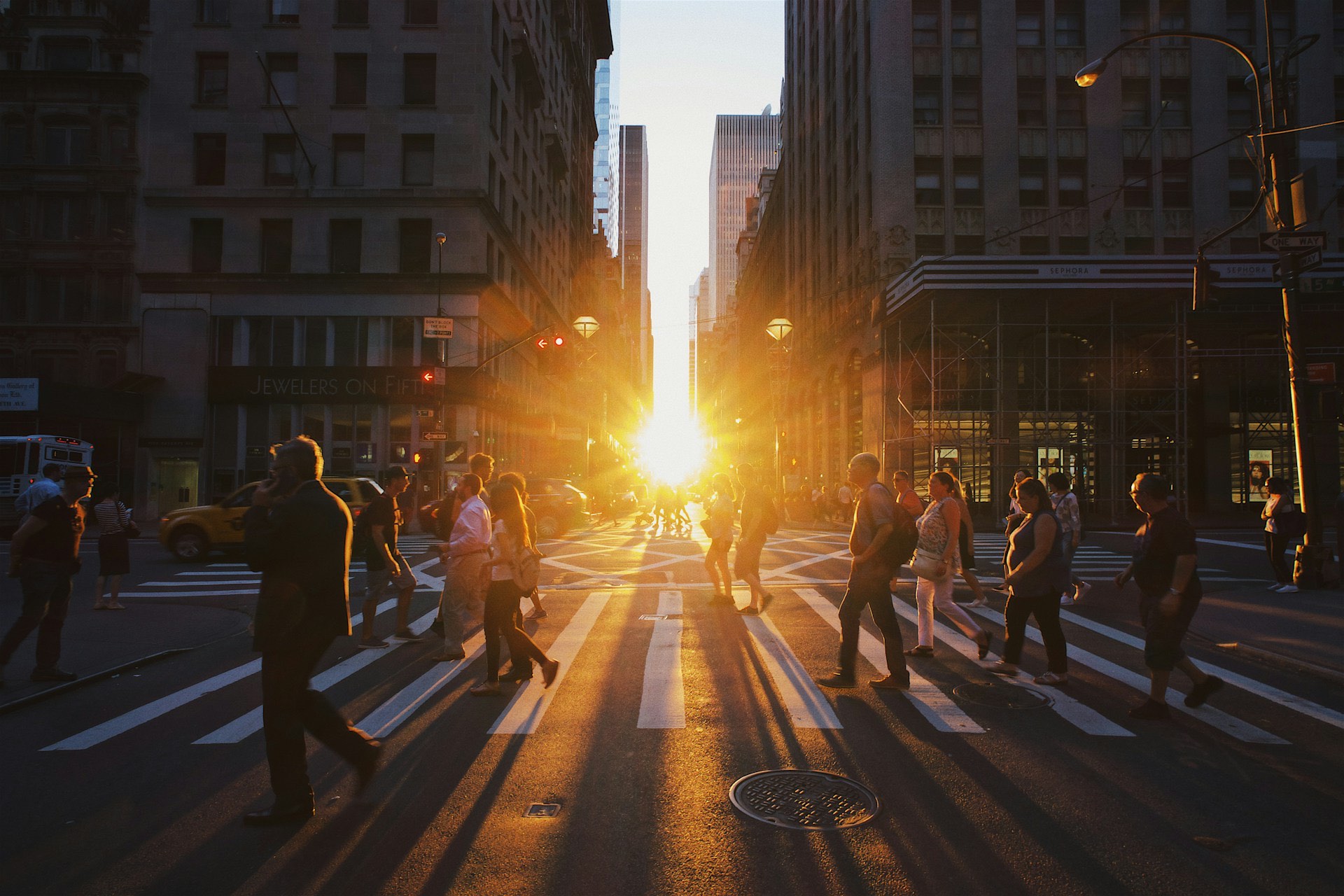 Crowds crossing a Manhattan street as the sun sets between the buildings
