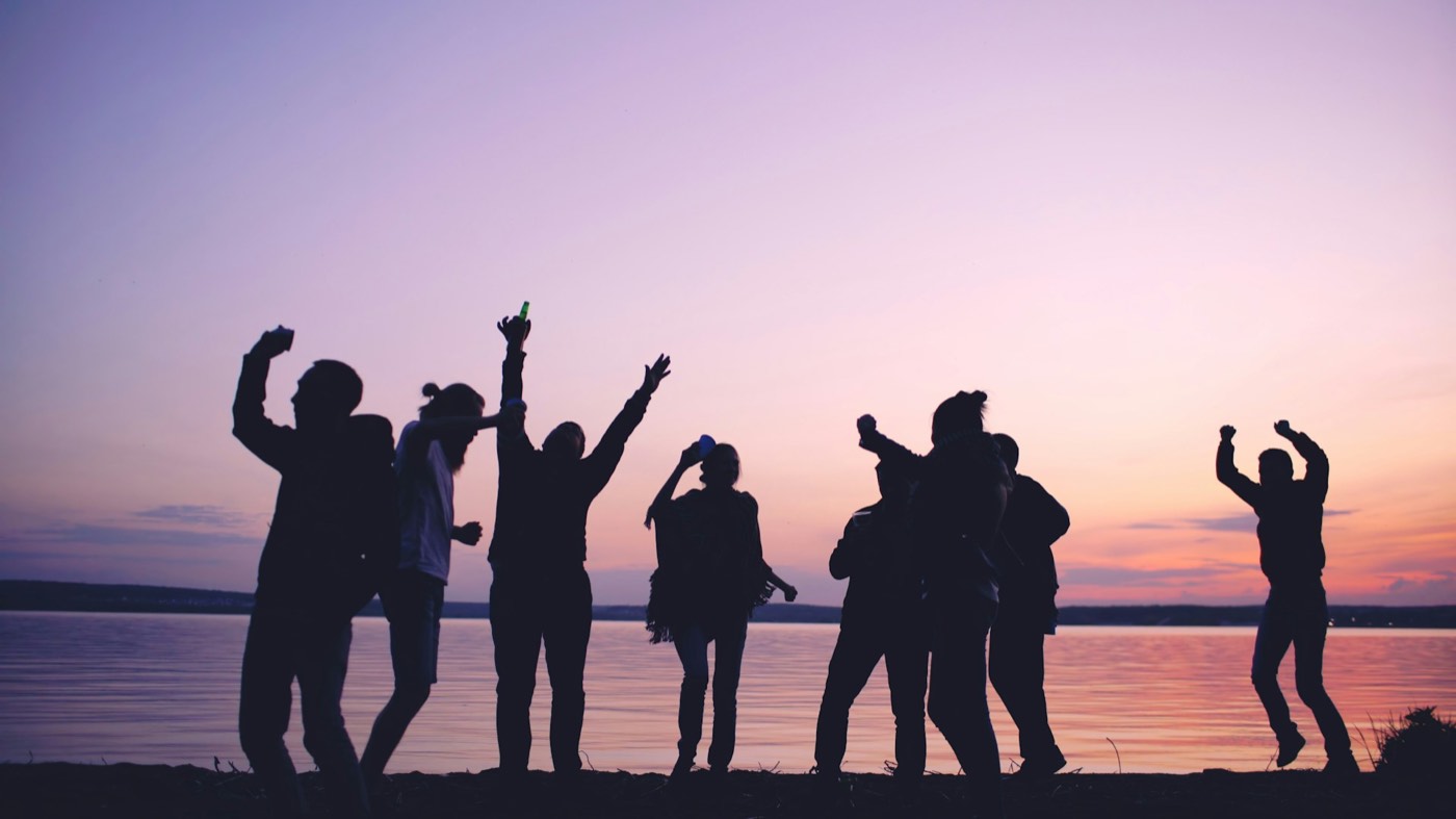 Silhouettes of young people celebrating against a sunset sky