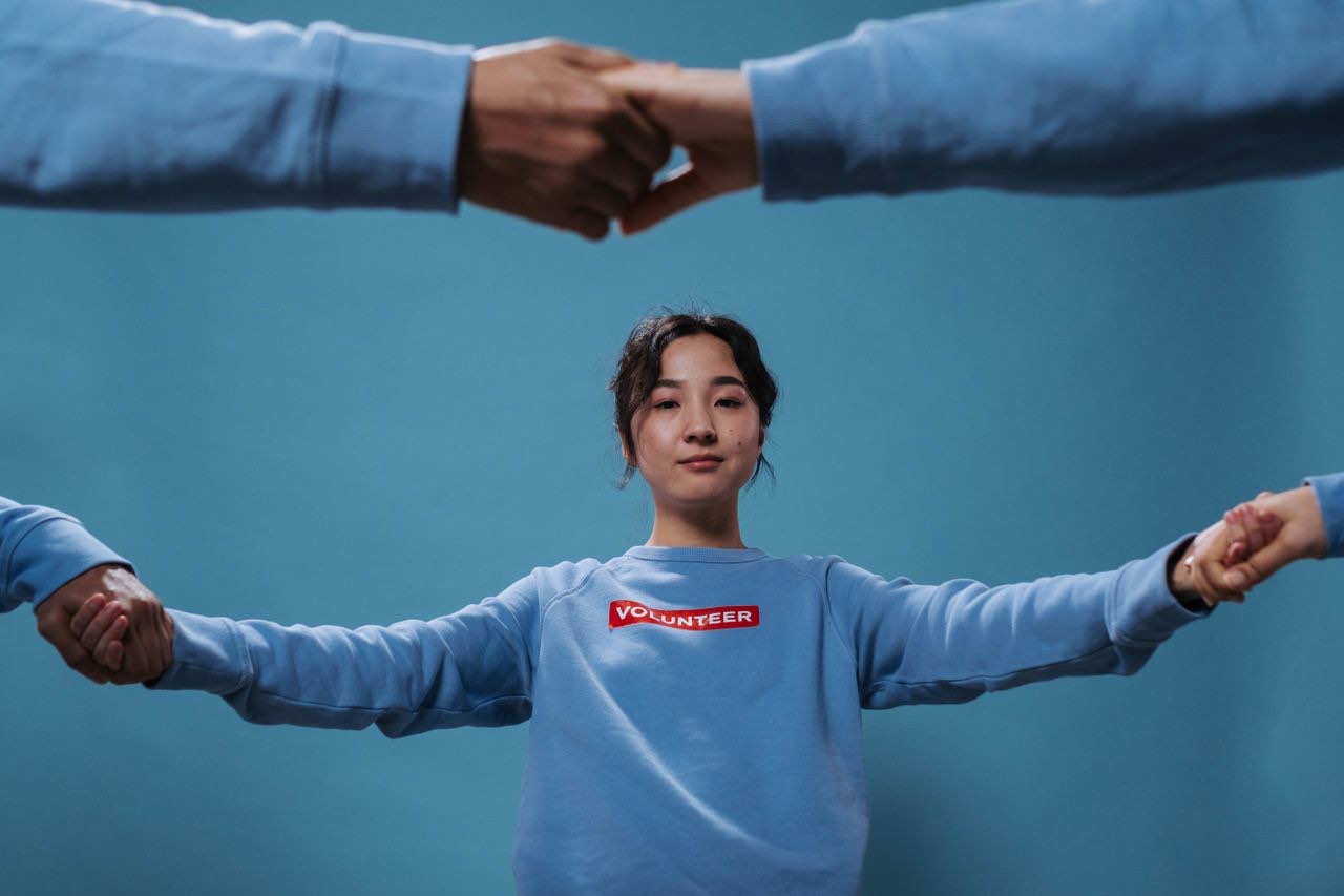 A young volunteer standing with arms outstretched, holding hands with people on either side