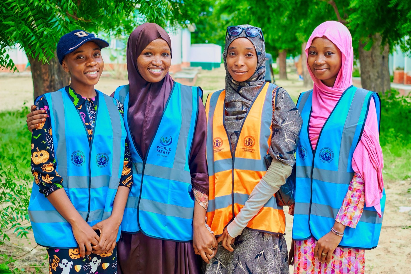 Four young women in volunteer vests smiling together outdoors